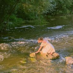 a woman standing on top of a rock in a river