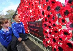 two children sitting next to a wall with red flowers on it