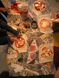 several people are making pizzas at a table with various toppings and condiments