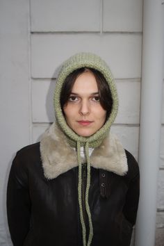 a woman wearing a hat and scarf in front of a white wall with a black leather jacket