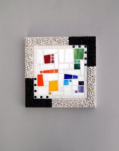 a piece of art that is made out of different colored squares and pebbles on a gray surface