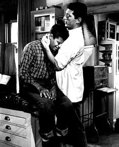 black and white photograph of two men sitting on top of a counter in a kitchen