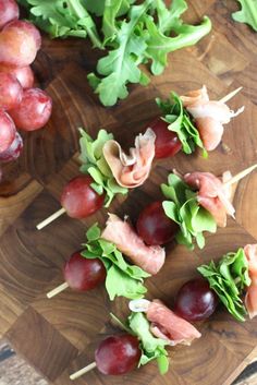 grapes and meat skewers on a wooden cutting board next to other food items