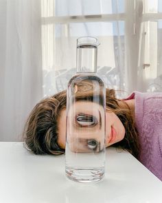 a woman laying her head on a table next to a glass bottle with rocks in it