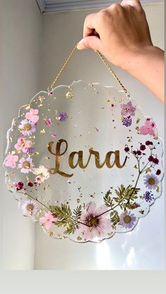 a person holding up a sign that says lara with flowers and leaves on it