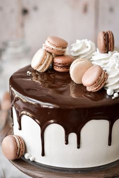 a chocolate cake with white frosting and macaroons on top, sitting on a wooden table