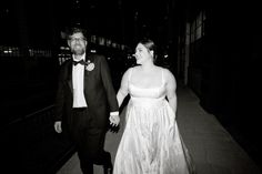 a bride and groom are walking down the street at night together, dressed in formal wear