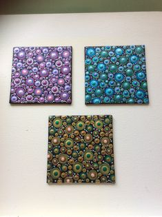 three square paintings on a white wall with blue, green and purple beads in them