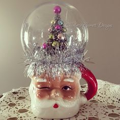 a snow globe with a santa claus head and christmas decorations on it, sitting on top of a doily