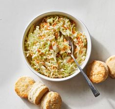 a bowl filled with coleslaw next to biscuits on a white surface