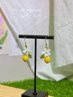 a pair of yellow and white crocheted pineapple earrings on a black stand