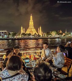 people sitting at tables in front of the water with food and drinks on each table