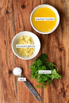 ingredients for homemade buttered garlic in small bowls on a wooden table with spoons