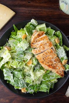 a salad with chicken and lettuce in a black bowl on a wooden table