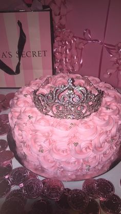 a pink cake with a tiara on top surrounded by coins and confetti