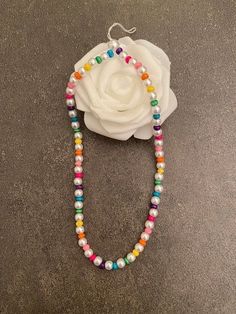 a white rose with multicolored beads and a beaded necklace on a gray surface