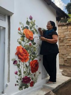 a woman painting flowers on the side of a building