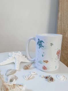 there is a coffee cup with sea shells on the table