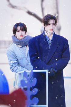 two young men standing next to each other in the snow wearing coats and scarfs