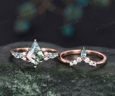 two rings with green and white stones on them sitting on a rock next to each other