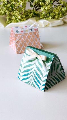 two small gift bags sitting on top of a white table next to green and pink flowers