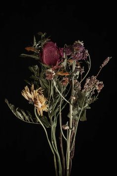 a vase filled with lots of flowers on top of a wooden table next to a black wall