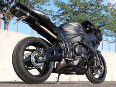 a black motorcycle parked on the side of a road next to a wall and trees