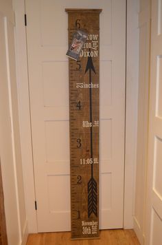 a wooden growth chart with an arrow on it in front of a white door and wood floor