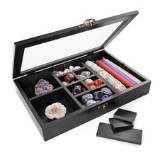 an open jewelry box with stones and candles in it on a white surface next to two black coasters