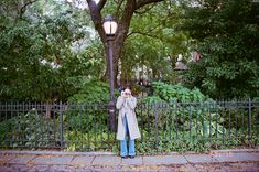 a woman taking a photo with her cell phone in front of a fence and street lamp