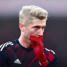 a close up of a soccer player holding his hand to his face while wearing red gloves