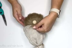 a person holding a stuffed animal in their hands with scissors and yarn on the table