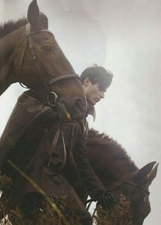 a man riding on the back of a brown horse next to a tall grass covered hillside