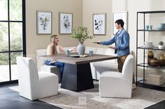 a man and woman sitting at a table in a living room with white chairs around them