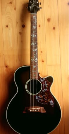 an acoustic guitar sitting on top of a hard wood floor next to a wooden wall