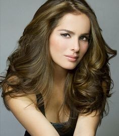 a beautiful young woman with long brown hair posing for a photo in front of a gray background