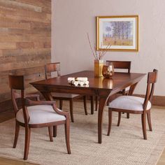 a dining room table and chairs in front of a wooden wall with a painting on it