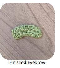 a green crocheted object sitting on top of a wooden table next to the words finished eyebrow