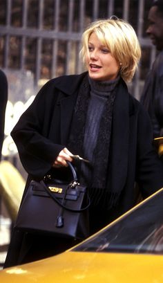 the blond woman is walking down the street with her hand in her pocket and holding a purse