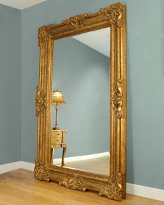 a large gold framed mirror sitting on top of a wooden floor next to a lamp