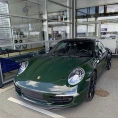 a green sports car is parked in front of a building with glass doors and windows