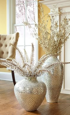 two white vases with plants in them on a wooden floor next to a chair