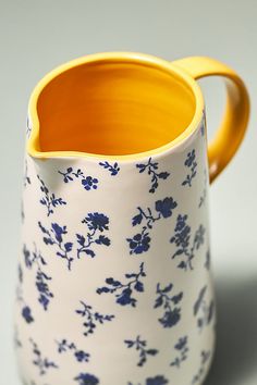 a blue and white flowered pitcher sitting on top of a gray surface with yellow rim