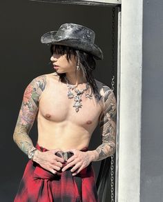 a shirtless man wearing a red and black plaid kilt with tattoos on his chest