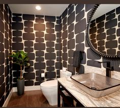 a bathroom with black and white wallpaper, a round mirror, sink and toilet