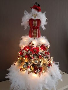 a red and white christmas tree with lights on it's top, surrounded by feathers