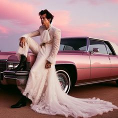 a woman in a wedding dress leaning on the hood of a pink car while wearing black cowboy boots