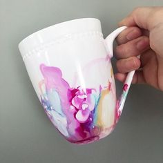 a hand holding a white coffee cup with pink and blue paint on it