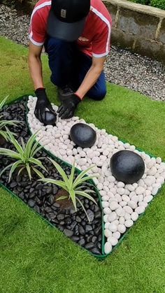 a man kneeling down next to a garden with rocks and plants in it on the grass