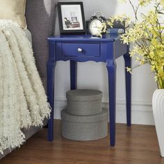 a blue table with a clock on it next to a gray ottoman and yellow flowers